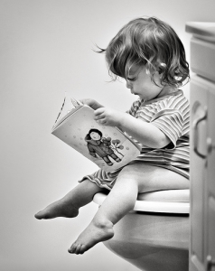 toddler girl sitting on toilet reading book