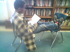 boy sitting on chair in library, reading a book