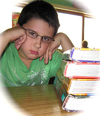 boy frowning near pile of school books