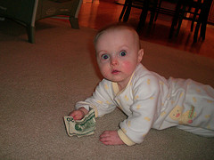 baby laying on floor holding twenty dollar bill