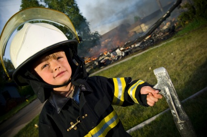 young boy wearing firefighter gear in front of burned out building