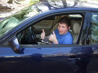 boy behind wheel of car showing two thumbs up