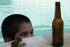 boy in pool looking longingly at beer bottle