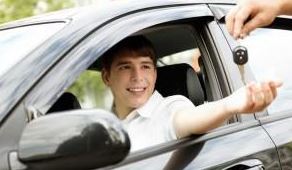 teen boy smiling in driver's seat as adult hands him car keys