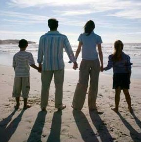 two parents and two children standing on beach, facing the water