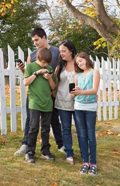 parents hugging two children who are holding cell phones