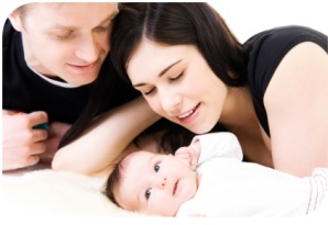 man and woman leaning over infant laying on bed