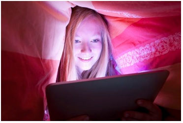 teen girl using computer under covers