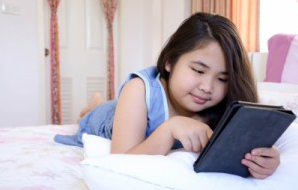 teen girl lying on bed looking at iPad