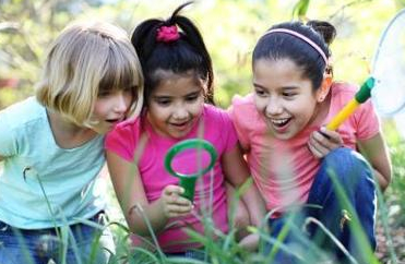 3 girls looking through magnifying glass at grass